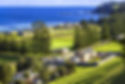 Aerial view of Kingston and Arthur’s Vale Historic Area on Norfolk Island, Australia, showcasing well-preserved colonial-era buildings, green rolling fields, tall Norfolk pine trees, and the deep blue waters of the Pacific Ocean in the background.