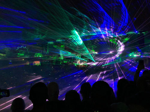 Crowd dancing in front of a grand, illuminated stage at Tomorrowland Festival in Belgium, with vibrant lights and electronic music.