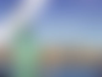 A low-angle shot of the Statue of Liberty with a bright blue sky and a few clouds overhead. The Statue of Liberty is in the foreground, with her iconic torch and tablet. The Manhattan skyline is visible across the water in the background, with the Hudson River separating the two. A diagonal purple banner with the words "Maximize Your NYC Adventure: Top Tips USA" is placed over the top left corner of the image.