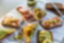 Assortment of Danish smørrebrød (open-faced sandwiches) topped with ingredients like salmon, shrimp, avocado, and mustard sauce, served on dark rye bread on a white parchment surface.