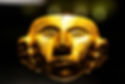 A detailed gold mask artifact displayed at the Museo del Oro (Gold Museum) in Bogotá, Colombia. The pre-Columbian piece features intricate facial carvings and symmetrical patterns, highlighting the craftsmanship of indigenous Colombian cultures. The artifact is illuminated against a dark background to emphasize its brilliance.