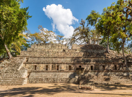 High-angle view of ancient Maya stone ruins surrounded by a dense green forest, featuring decorative text overlays.