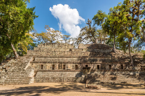 Ancient stone Maya pyramid structure at the Acropolis in Copán with small windows and surrounding lush green trees.