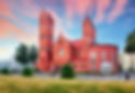 The Red Church, also known as the Church of Saints Simon and Helena, located at Independence Square in Minsk, Belarus, glowing under a colorful sunset sky.
