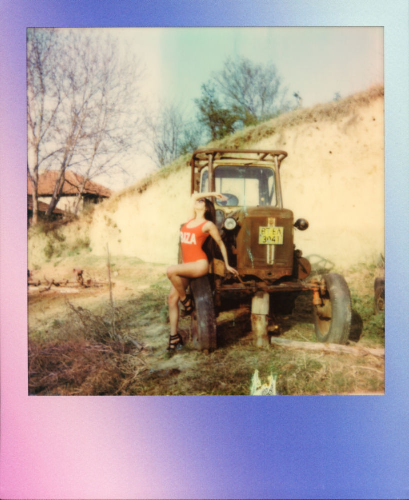A Polaroid of Misuzu in a swimsuit leaning on a broken-down tractor