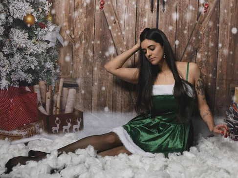 Misuzu in an elf dress from the waist up, sat in front of a festive back drop surrounded by fake snow