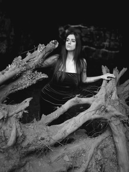 Monochrome of Misuzu wearing a purple velvet dress, stood behind a large fallen tree