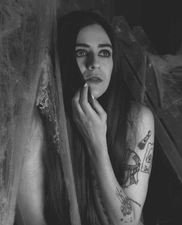 Monochrome of Misuzu in a set full of cobwebs. She is huddled up looking scared at something off camera
