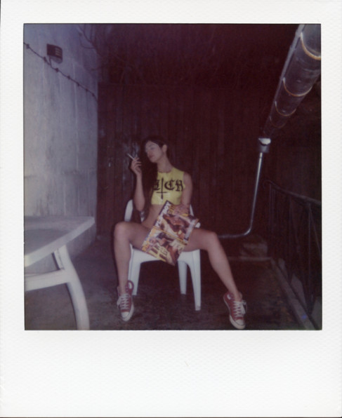 A Polaroid of Misuzu wearing a latex top saying 'bitch', smoking and holding a copy of a Playboy magazine