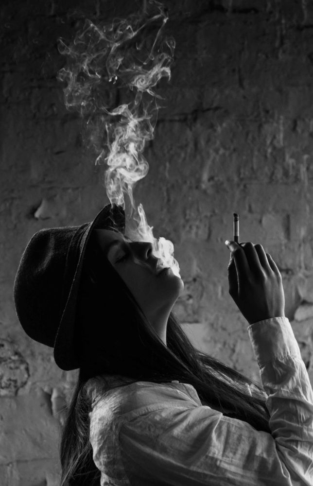 Monochrome of Misuzu wearing a black hat and white shirt. She is smoking and has her head back.