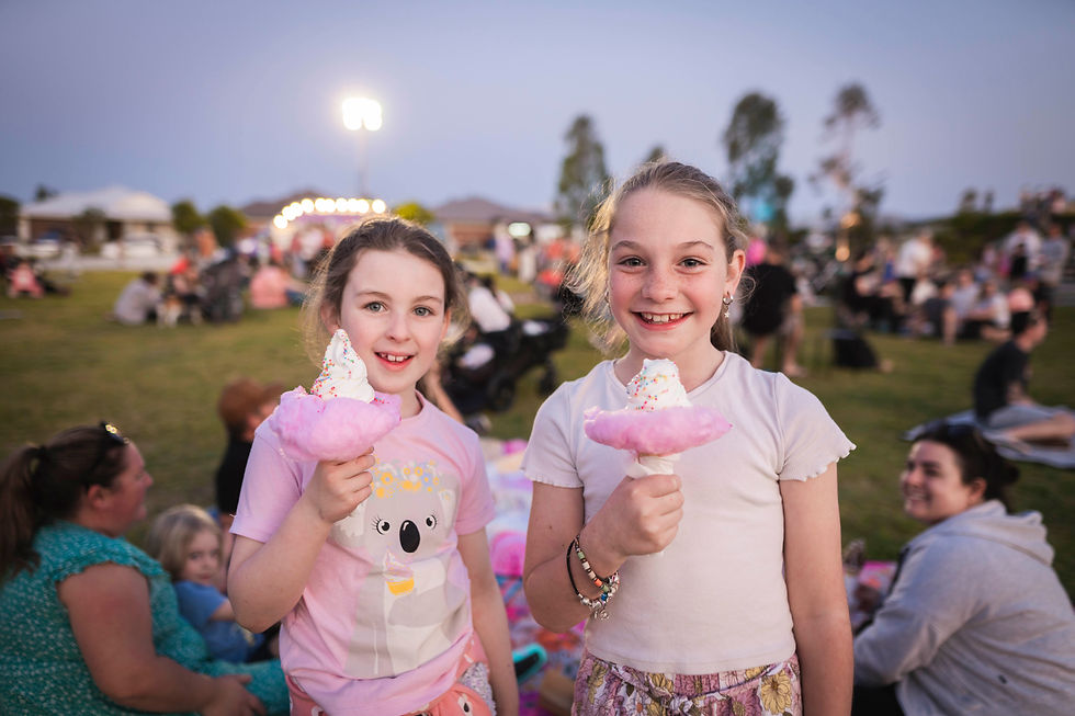 Two smiling girls holding pink cotton candy with ice cream. They are outdoors at an event, with a crowd and lights in the background.