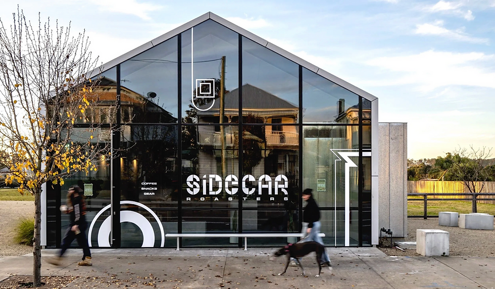 Glass-fronted café "Sidecar Roasters" with reflections of buildings. People walk by with a dog. Yellow leaves on trees. Text: Coffee, Snacks.