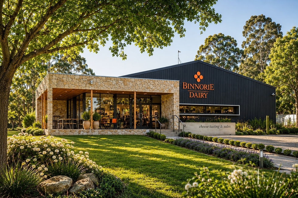 Modern Binنورie Dairy building with stone facade and garden lawn, orange sign, and cheese tasting & sales text in sunny treeskip setting
