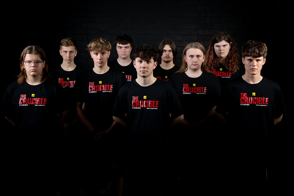 A group of nine people wearing black "The Crucible" T-shirts stand against a dark background, looking serious and focused.