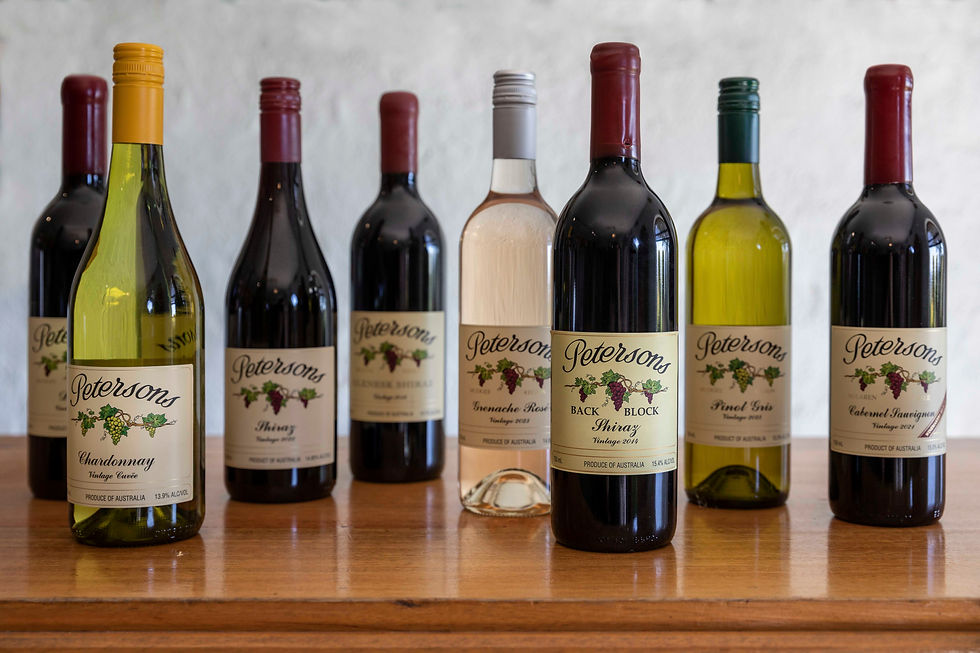 Seven Petersons wine bottles on a wooden table, with labeled Chardonnay, Shiraz, Rosé, Pinot Gris, and Cabernet Sauvignon bottles.