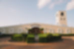 Beige winery with "Bimbadgen" text, tower, and arched windows. Green hedges and fountain in the foreground, under a clear sky.