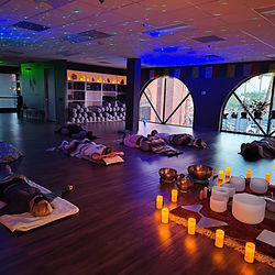 A peaceful healing space with mats, blankets, and knee bolsters placed near singing bowls. The room features arched windows, natural lighting and a warm ambiance.