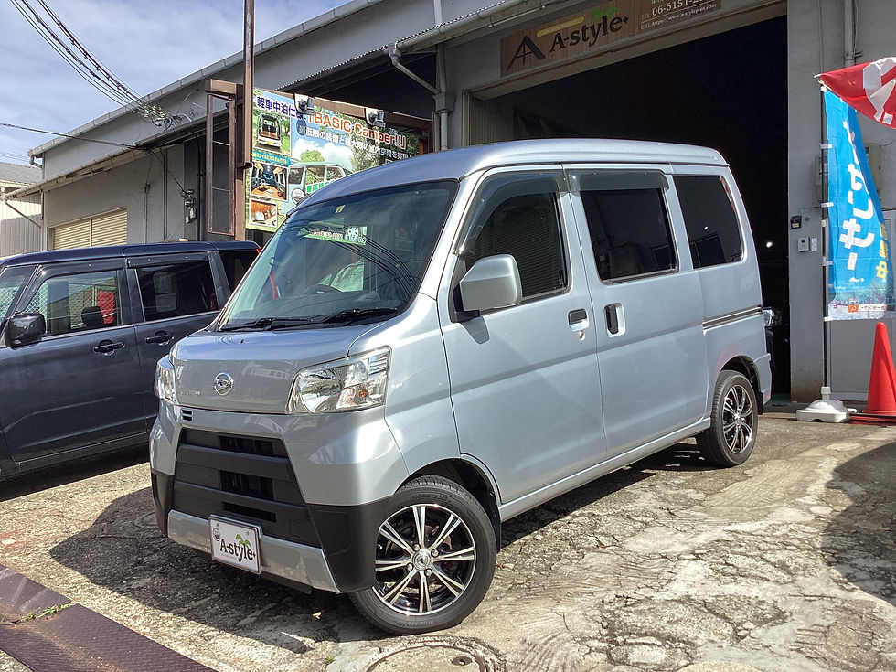 A-stylePlusの店先に停まる銀色の軽バン。キャンピング仕様の案内看板と青いのぼりが見える晴れた日。