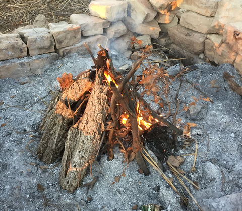Campfire burning with stacked logs inside a stone fire pit in West Texas.