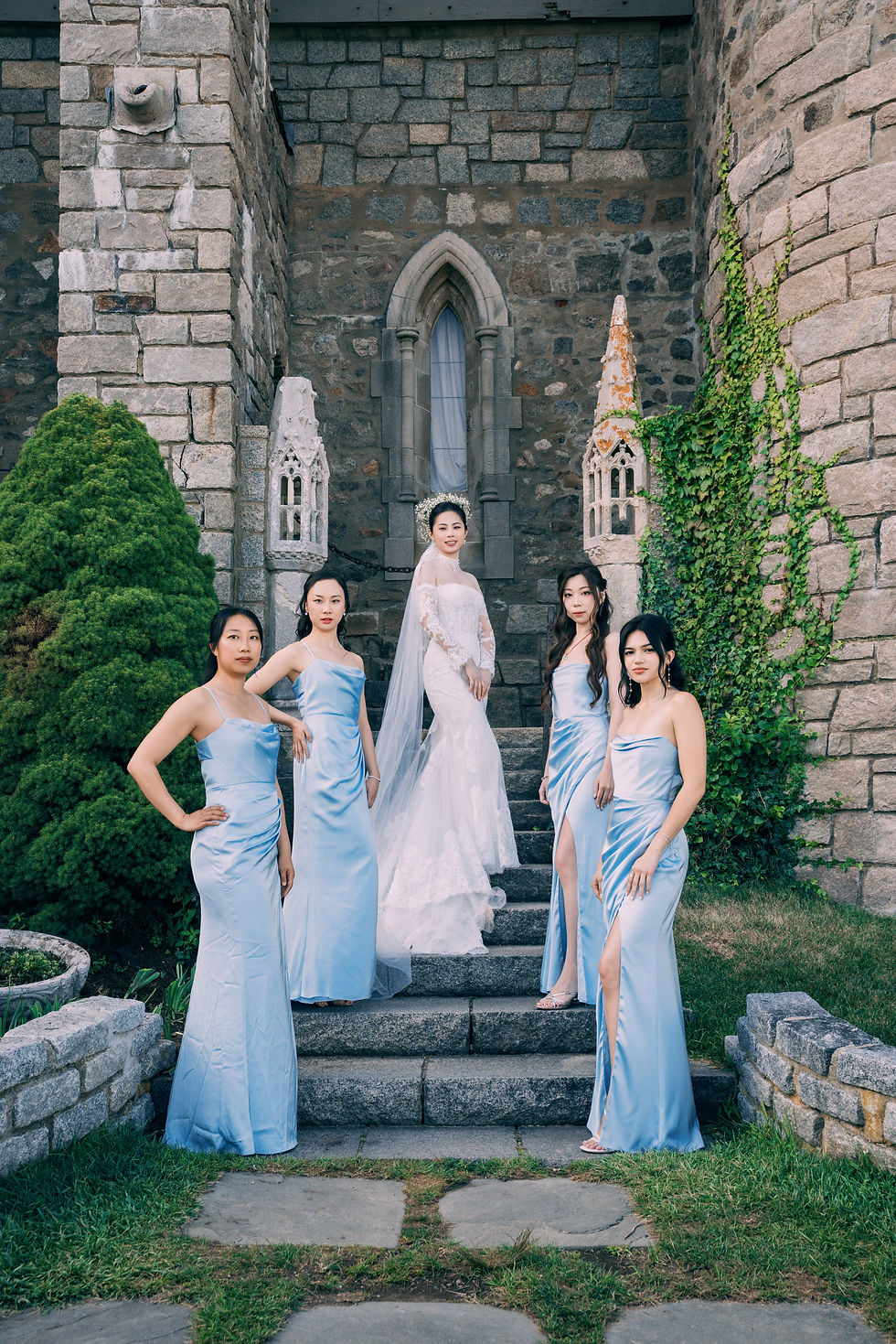 Bride and bridesmaids in dusty blue on the stone steps of Hammond Castle