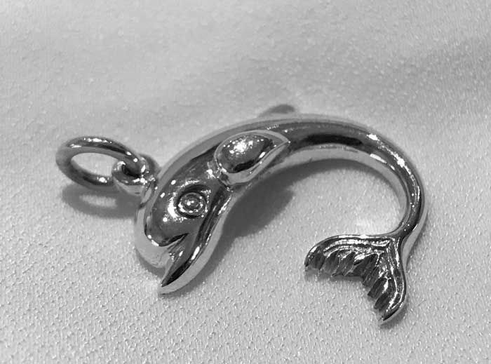 Small silver dolphin pendant laying on a white surface