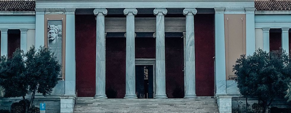 The National Archaeological Museum of Athens, Greece, featuring a grand neoclassical facade with towering columns, statues on the rooftop, and a Greek flag waving above the entrance.