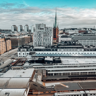 A panoramic view of Stockholm's modern and historic architecture, featuring the city skyline with a train station in the foreground and a church spire in the background.