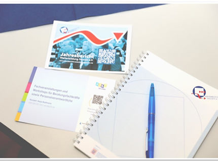 Foto eines Tagungstisches bei der Mitgliederversammlung von Weiterbildung Hessen. Zu sehen sind Seminarunterlagen, ein Notizblock mit Kugelschreiber sowie Materialien mit QR-Codes und dem Logo von Weiterbildung Hessen.