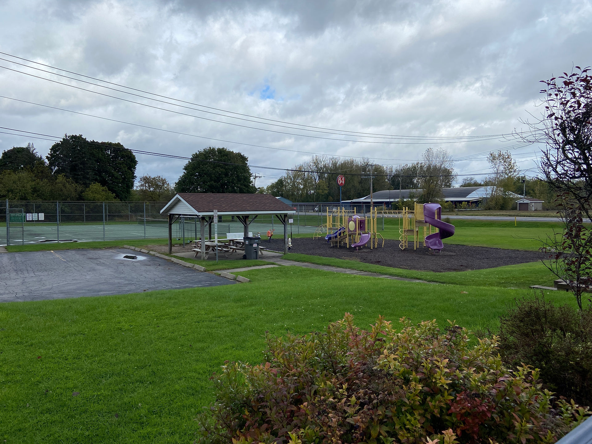 A distant photo of a purple and yellow swing set with a spiral slide. Small wooden pavilion in the foreground.