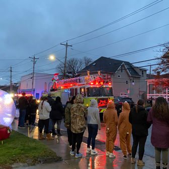 A fire truck passes decorated with holiday lights drives by as people watch.