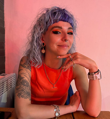 an image of kaytie who has blue hair and is wearing a red top with her hand under her chin