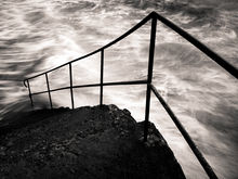 Un escalier de pierre et une rampe en metal se jettent dans la mer agitée.