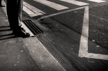 Un homme au pantalon en tweed et des souliers en cuirs attend de traverser la route.
