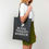 Thumbnail: Woman holding a dark gray tote bag that says "Retail Therapy Warrior"