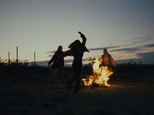 Silhouettes of people dancing around a fire.