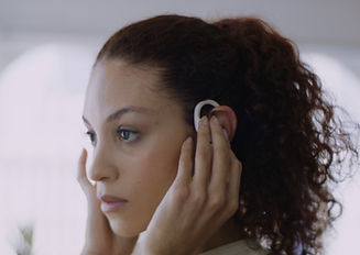 A Black woman turning on music in her pink wireless earphones.