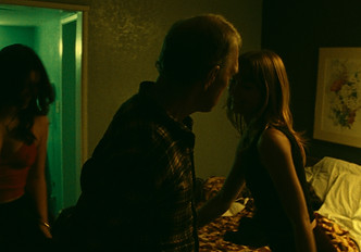 Two people kissing on the bed of a motel room.