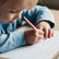 A young child writing on paper with a pencil.