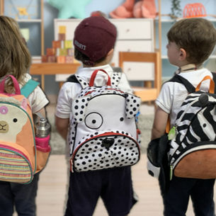 A line of children wearing animal backpacks walking into a classroom.