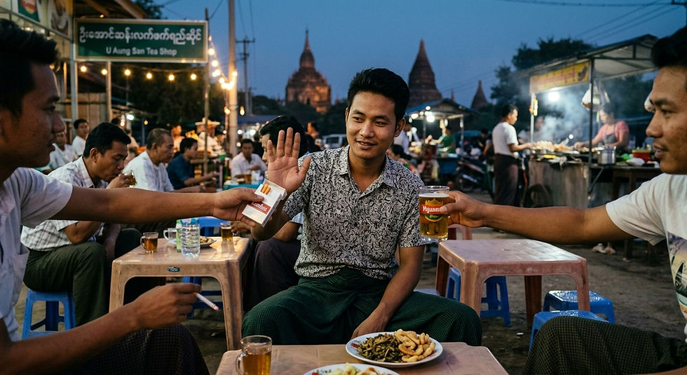 Men chat at dusk in a bustling outdoor tea shop, one waving as friends offer a cigarette and beer under a U Aung San Tea Shop sign.