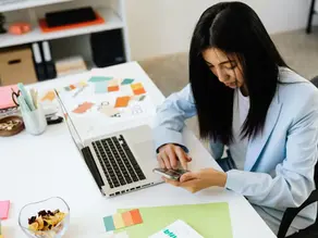 Person sitting at a desk looking overwhelmed while working on a laptop and phone, representing workplace burnout and chronic stress.