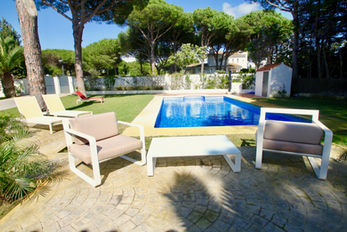 Loungers by blue-tiled pool surrounded by pines.