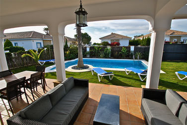 Covered veranda with seating area, garden view and terracotta flooring.