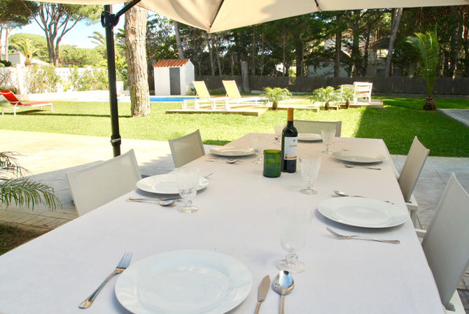 Large dining table under parasol surrounded by lawn and plants.