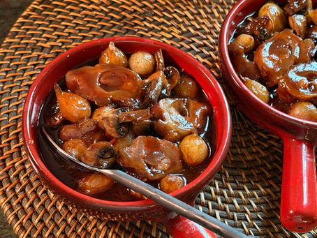 Red terracotta bowls with beef tendon stew featuring mushrooms and pearl onions on a woven mat. Rich brown sauce, reflecting warm light, evokes a cozy feel.