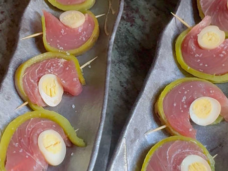 Slices of raw fish layered with Hatch and quail eggs on toothpicks, served on rustic gray plates.