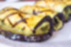 Grilled eggplant rolls stuffed with Georgian style walnut filling on a white plate. The eggplant has dark grill marks and a glossy, purple skin.