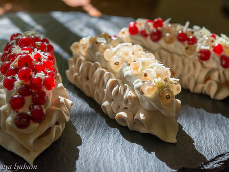 Pavlova Pastries. Three meringue desserts topped with red and white currants on a slate surface, lit by soft sunlight. Moody and artistic presentation.