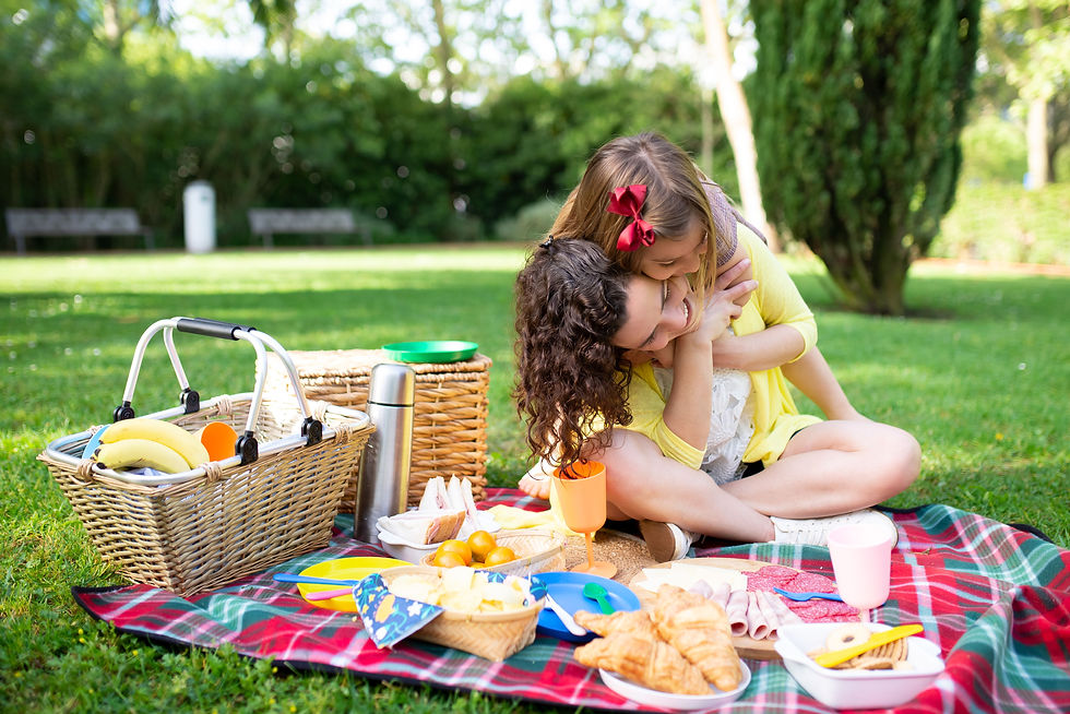 Mother and daughter enjoying a summer picnic in a park, sharing a hug on a blanket with a picnic basket and snacks.