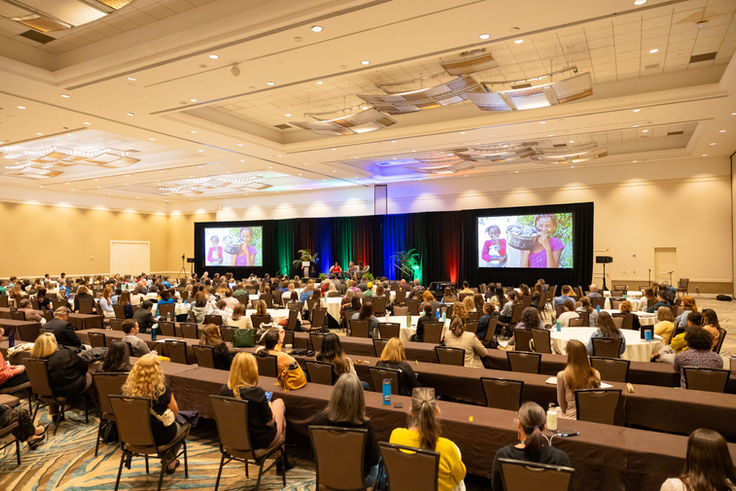 Wide-angle view of a keynote session at the ADAPT Conference in Orlando, Florida, with attendees seated in rows, stage lighting, and dual screens displaying speakers.